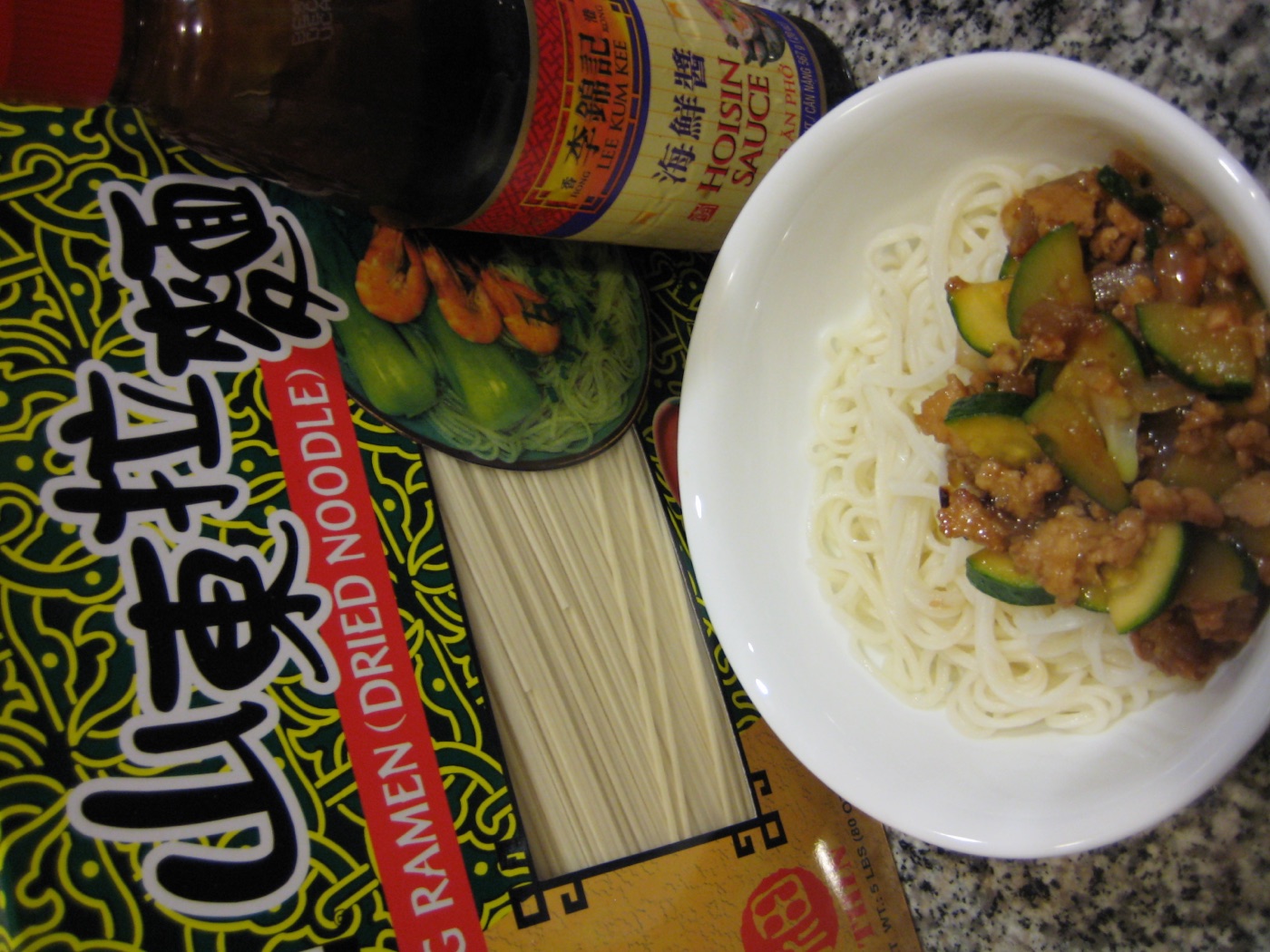 Hoisin sauce, dry noodles behind a bowl of the completed hoisin pork on noodle dish